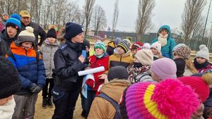 Policjantka trzyma w rękach ulotki i informuje dzieci o trwającym konkursie.