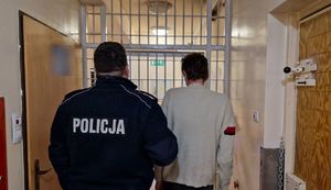 Umundurowany policjant stoi z zatrzymanym mężczyzną.