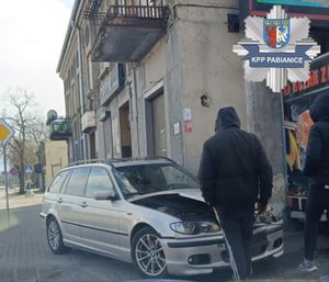 Mężczyźni stoją przy uszkodzonym w wyniku zdarzenia drogowego bmw.