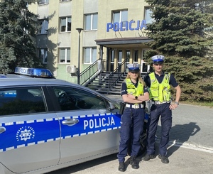 policjant i policjantka stoją przy radiowozie przed komendą