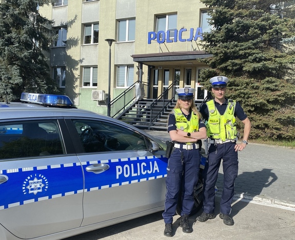 policjant i policjantka stoją przy radiowozie przed komendą