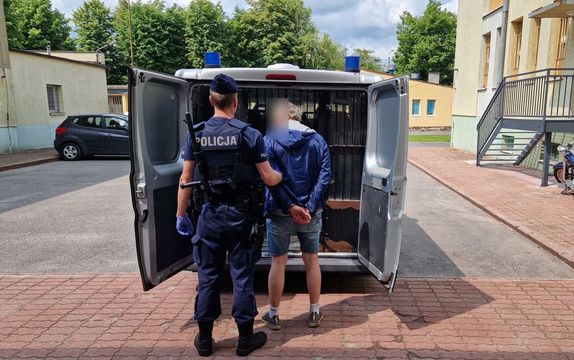 Umundurowany policjant stoi z zatrzymanym mężczyzną.