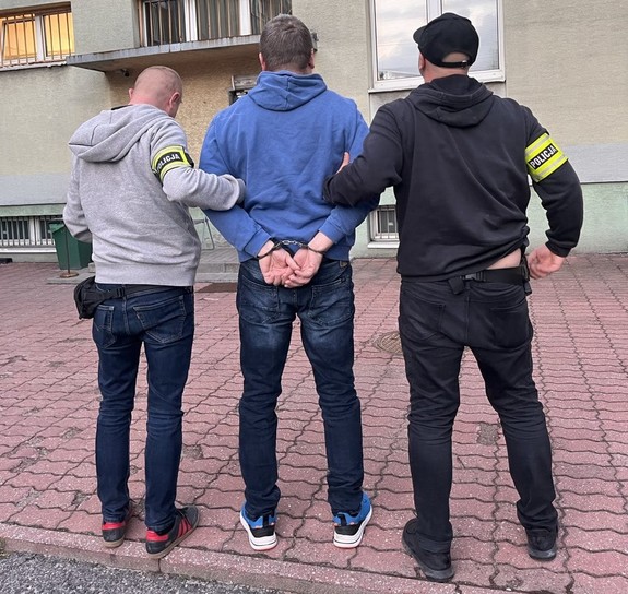 Policjanci prowadzą do komendy poszukiwanego listem gończym mężczyznę.