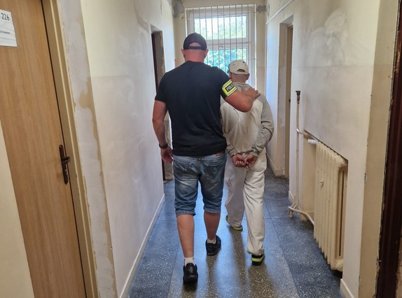 Nieumundurowany policjant prowadzi zatrzymanego mężczyznę.