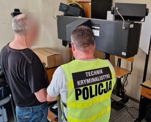 Technik kryminalistyki pobiera odciski palców zatrzymanemu mężczyźnie.