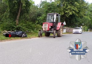 Miejsce zdarzenia drogowego, na którym widać stojący ciągnik rolniczy i przewrócony motocykl.