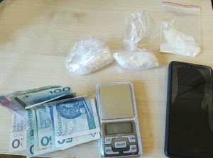 Trzy woreczki foliowe z białym proszkiem, mała waga, telefon komórkowy oraz pieniądze w banknotach.