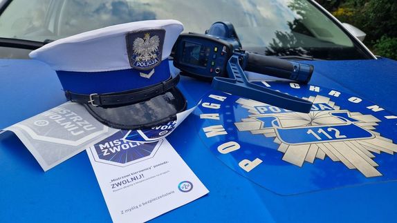 Leżące na radiowozie: policyjna czapka, ulotka, naklejki i miernik prędkości.