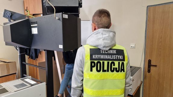 Policjant stoi przy urządzeniu do fotografowania zatrzymanych.