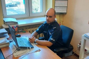 Umundurowany policjant siedzący za biurkiem.
