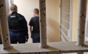 Policjantka z zatrzymanym mężczyzną stoją za kratami policyjnej celi.
