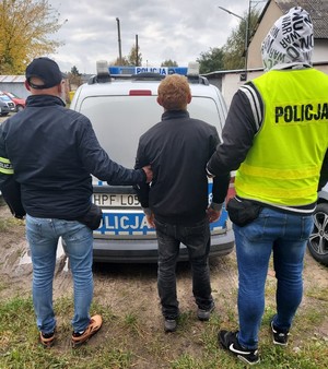 Nieumundurowani policjanci stoją z zatrzymanym mężczyzną.
