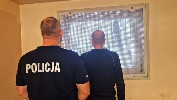 Umundurowany policjant stoi z zatrzymanym mężczyzną.