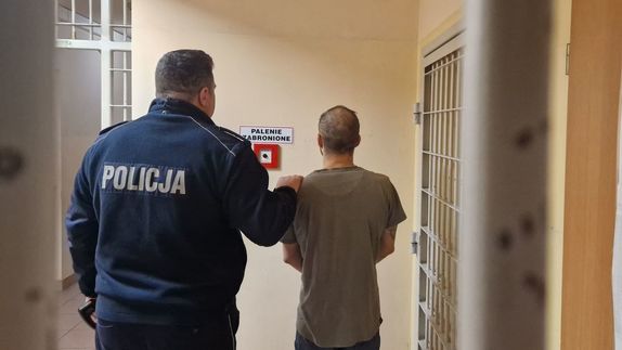 Umundurowany policjant stoi z zatrzymanym mężczyzną.