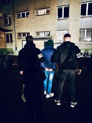 Kryminalni stoją z zatrzymanym mężczyzną.