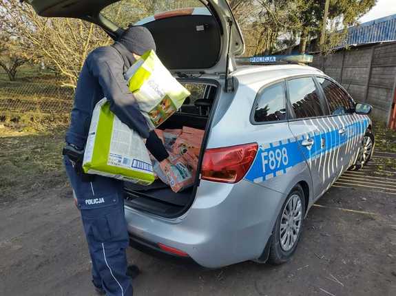 Policjant wyciąga z bagażnika radiowozu karmę dla zwierząt.