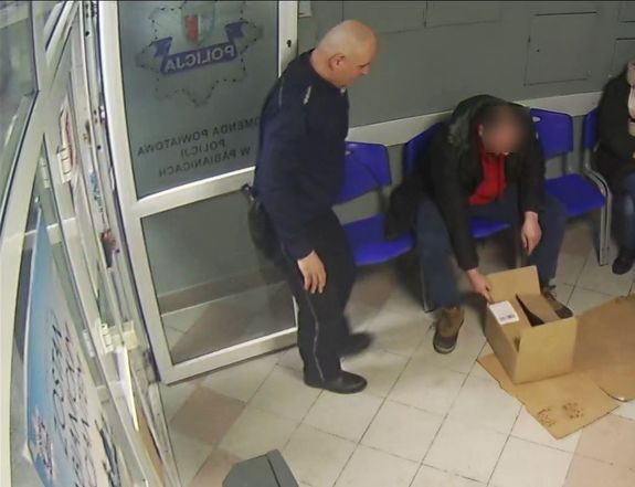 Mężczyzna pokazuje policjantowi zawartość kartonowego pudła.