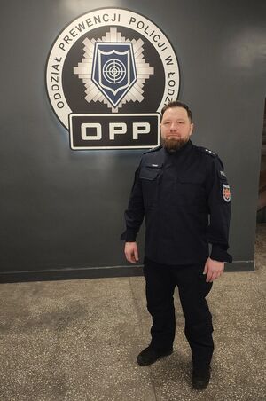 Policjant na tle logo Oddziału Prewencji Policji w Łodzi.