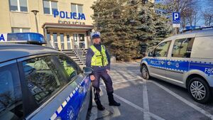 Policjant stoi pomiędzy oznakowanymi radiowozami.