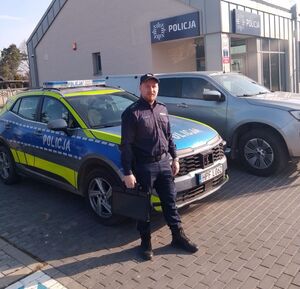 Dzielnicowy stoi przy radiowozach.