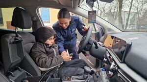 Chłopiec siedzi w radiowozie, policjantka pokazuje mu jak użyć sygnałów świetlnych i dźwiękowych.