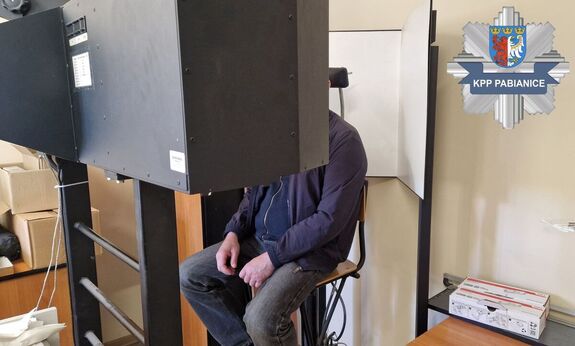 Podejrzany siedzący na urządzeniu do wykonywania zdjęć przez techników kryminalistyki znajdujący się w trakcie procedury fotografii sygnalitycznej.