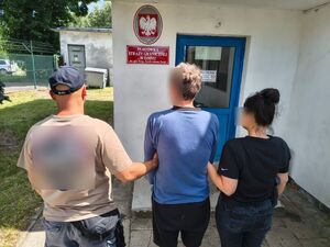 Nieumundurowani policjanci stoją z podejrzanym przy drzwiach placówki straży granicznej.
