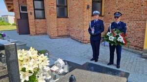 Komendant Powiatowy Policji w Pabianicach trzyma w ręku wiązankę biało-czerwonych kwiatów, obok niego znajduje się Naczelnik Wydziału Ruchu Drogowego Komendy Powiatowej Policji w Pabianicach. Obaj stoją przed grobem zmarłego policjanta.