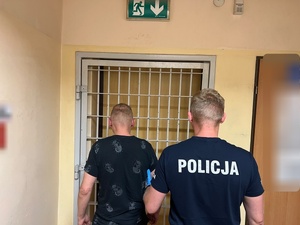 umundurowany funkcjonariusz trzyma zatrzymanego
