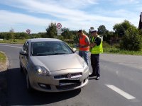 policjant z pracownikiem PKP stoi przy aucie i wręcza kierowcy ulotke