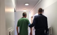 Policjant prowadzi zatrzymanego do celi
