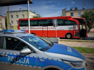 Radiowóz policyjny, a na drugim planie bus krwiodawstwa.