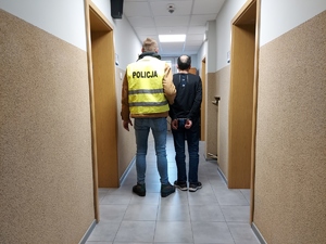 Policjant prowadzi podejrzanego korytarzem