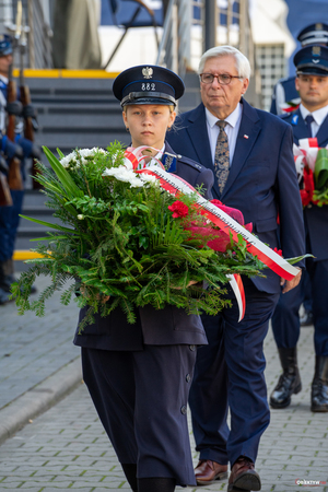 Na zdjęciu widoczna jest kobieta w mundurze policjantki z okresu II RP niosąca kwiaty