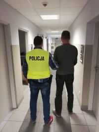 Policjant prowadzi zatrzymanego mężczyznę.