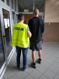 Policjant prowadzi zatrzymanego mężczyznę.