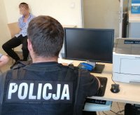 Policjant siedzi przed komputerem, przed nim siedzi zatrzymany mężczyzna.