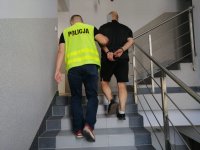 Policjant prowadzi zatrzymanego mężczyznę.