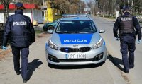 Dwaj umundurowani policjanci podchodza do oznakowanego radiowozu, sa tyłem.