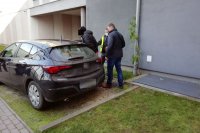 Nieumundurowani policjanci prowadzą zatrzymanego mężczyznę do zaparkowanego nieoznakowanego samochodu