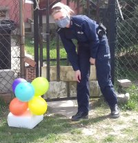 umundurowana policjantka zostawia tort urodzinowy z balonami pod domem