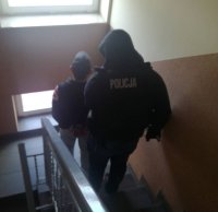 Policjan z kamizelką z napisem Policja prowadzi zatrzymanego mężczyznę po schodach