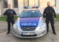 umundurowani policjanci stoją przy oznakowanym radiowozie