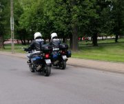 dwaj umundurowani policjanci w białych kaskach na głowie jadą motocyklami po drodze