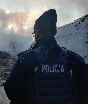 Umundurowany policjant stoi przed unoszącym się dymem