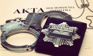 Akta sprawy leżą na biurku, na nich leżą kajdanki i odznaka policyjna - srebrna gwiazda z napisem Policja
