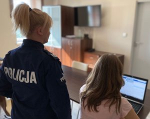 umundurowana policjantka stoi przy dziewczynie, która siedzi przed komputerem