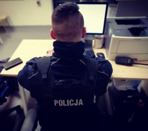policjant siedzi przy biurku, przed monitorem komputera