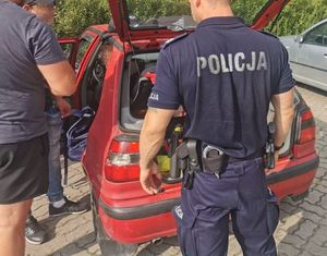 policjanci stoją przy samochodzie koloru czerwonego z otwartym bagażnikiem