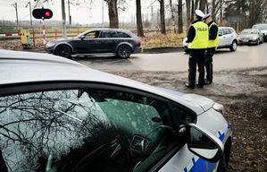 Dwóch policjantów w żółtych kamizelkach stoi na drodze gdzie przejeżdżają samochody.